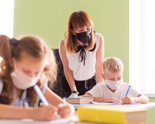 Maestros y niños protegiéndose con mascarillas en clase | Foto: Freepik 