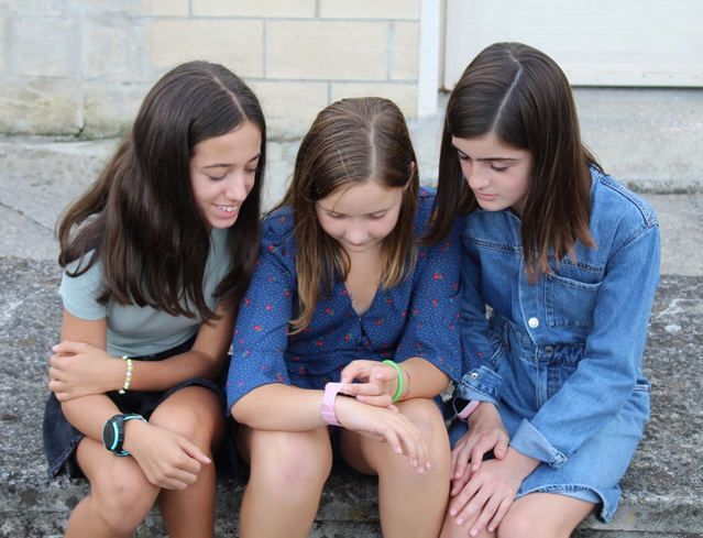 Tres niñas observando detenidamente un smartwatch con GPS.