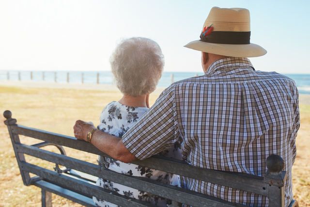 Una pareja de personas mayores sentadas sobre un banco a la orilla del mar.